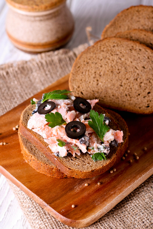 Smoked salmon and soft cheese spread, mousse, pate on a bread with olives and parsley, close up, vertical, top viewの写真素材