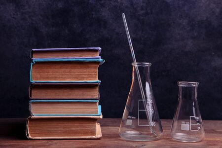 Stack of books and chemical flasks on wooden table on black background. Concept teacher's day, chemistry.の写真素材
