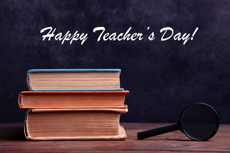 Stack of books and magnifier on wooden table on black background. Concept teacher's day. Copy space.の写真素材