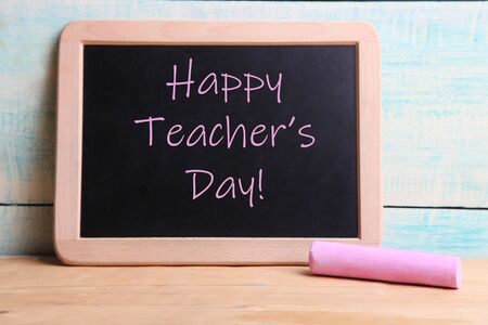 Chalk board and piece of pink chalk on wooden background. Concept teacher's day. Copy space.の写真素材
