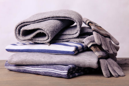 A stack of sweatshirts, a scarf and gloves on a neutral background.