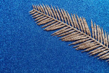 Artificial golden palm branch on a shiny blue background. Christmas concept.の写真素材
