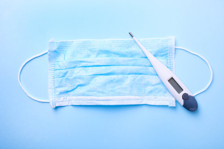 Blue medical mask with a thermometer on a blue background. Epidemic concept