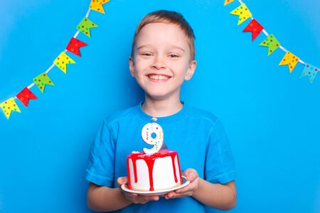 Happy boy holds a birthday cake on a blue background. Birthday concept.の写真素材