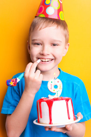 Happy boy in a festive cap is holding a cake on an orange background. Birthday concept.