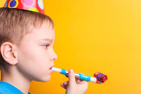 A boy in a festive cap blows into a pipe on an orange background.の写真素材