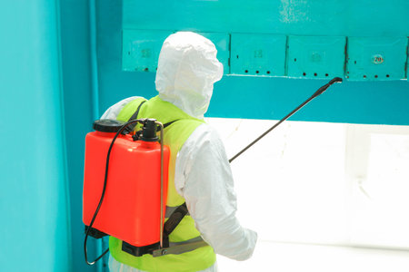 A specialist in a protective suit disinfects the entrance from a coronavirus infection. Epidemic...