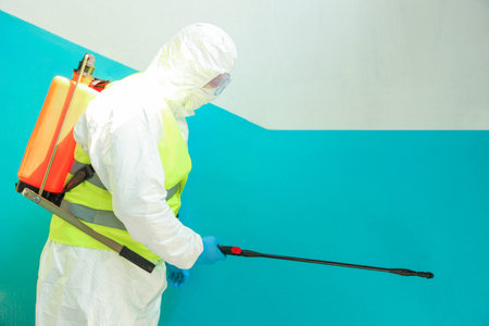 A specialist in a protective suit disinfects the entrance from a coronavirus infection. Epidemic...