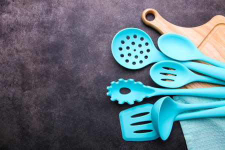 Set of blue nylon kitchen utensils and cutting board on a black background.