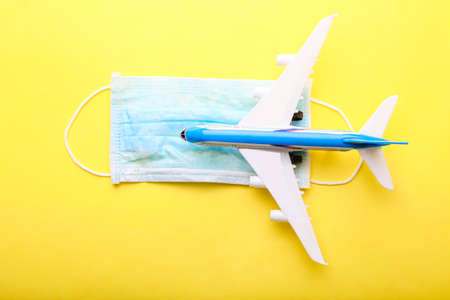 Toy plane and medical mask on a yellow background. Safe travel.の写真素材