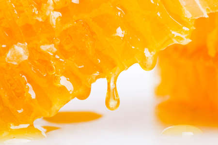 A drop of honey flowing down from the honeycomb close-up.の写真素材