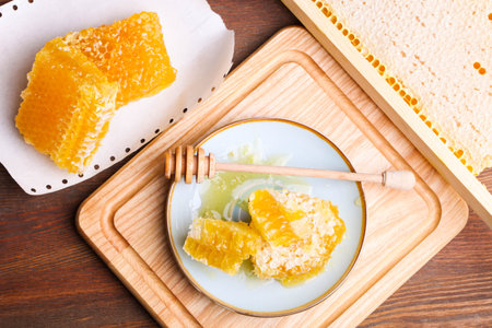 Golden cut honeycomb with a wooden spoon on cutting board on a brown background.