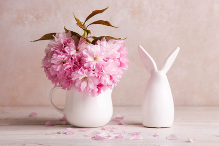 Figurine of Easter bunny and bouquet of pink sakura on white background.の写真素材