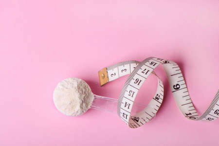 White protein powder in spoon and measuring tape on pink background.の写真素材
