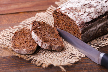 Loaf of rectangular rye bread on burlap on wooden brown background.