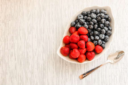 Blueberries and strawberries in a bowl on a neutral background.の写真素材