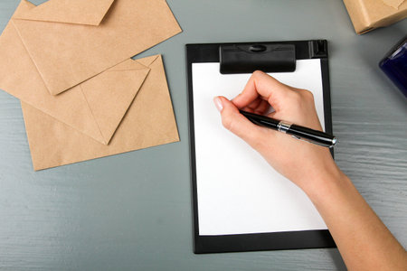 woman's hand writes on paper on gray wooden background. Craft envelopes with letters. Sending...
