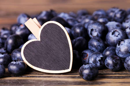 Ripe blueberries with decorative wooden heart on brown background.の写真素材