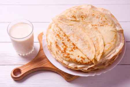 Stack of thin pancakes on plate and glass of milk on white wooden background. pancake weekの写真素材