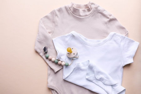 Baby bodysuit and pacifier with holder on beige background.