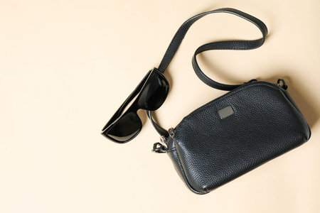 Black leather crossbody handbag with sunglasses on brown background.の写真素材