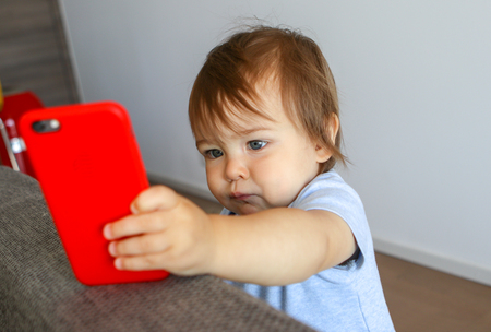Adorable little baby boy looking seriously at screen of mobile phone. Child and gadget conceptの写真素材