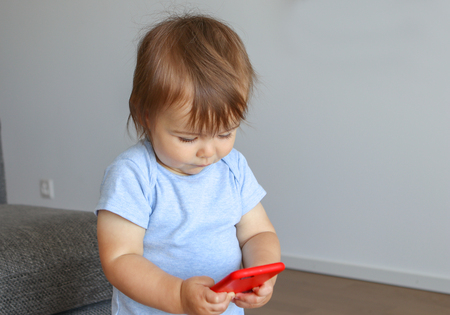 Cute little baby holds mobile phone in his hands and looking attentively at screen. Child and gadget, parent control concept.の写真素材