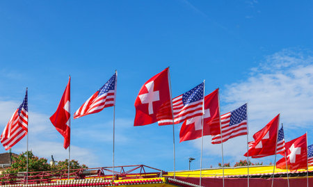 Ten american and swiss flags waving in row on blue sky background. USA and Switzerland flags