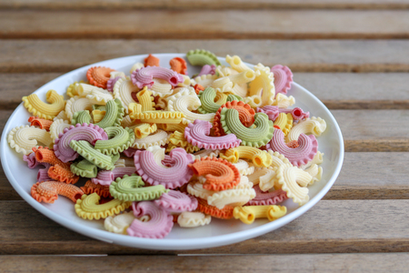 Colorful green, yellow, white, orange and pink italian crown pasta on white plate staying on wooden table, close-up.の写真素材