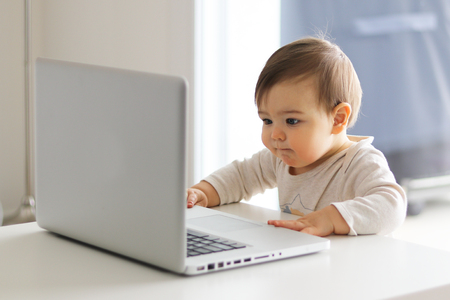little baby is looking attentively at the screen of laptop in front of him, working with computer.  Child and computer conceptの写真素材