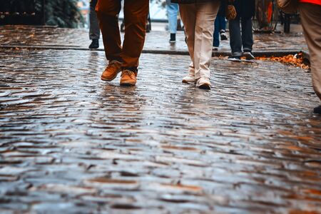 Front view at people feet in shoes walking on wet pavement at rainy autumn day. Copy space. Fall lifestyle. Man and woman walk together at rainy weather outdoors. の写真素材