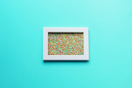 Mock up. White empty picture frame with colorful sprinkles inside on trendy neo mint paper...
