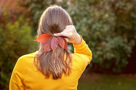 Autumn fashion accessories. Back view of romantic teenager girl  with bright red fall leaves hairpin in her hair. Natural bijouterie. Autumn lifestyle の写真素材