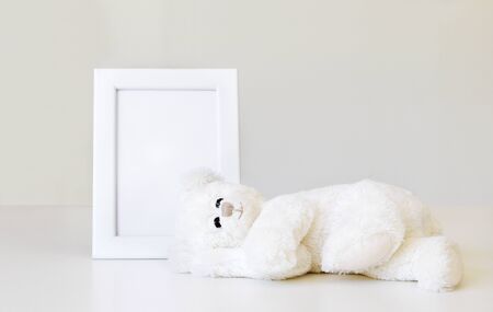 Mockup. Soft white little teddy bear toy sleeping near white clean mock up frame with copy space at light grey background. Empty space. Baby children concept. の写真素材