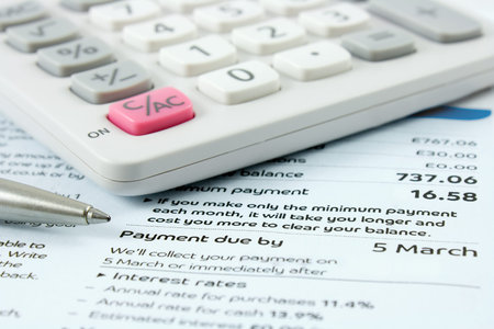 calculator and silver ballpoint pen sitting on a bank statement with focus on the payment due date