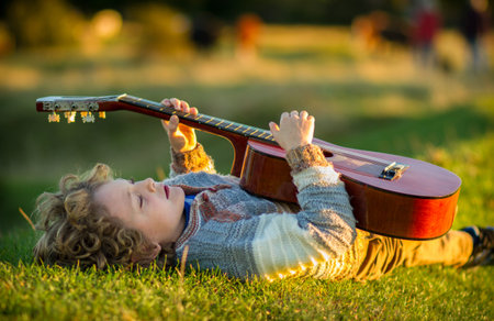 a 7 year old caucasian boy with blonde curly hair laying on his back on grass at sunset playing a...