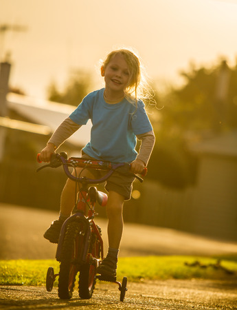 young child riding a bike with trainer wheels at sunsetの写真素材