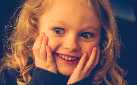 close up of a 4 year old caucasian child with blonde hair and blue eyes with chin in his hands looking surprised.の写真素材