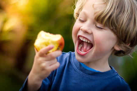 close up of 5 year old blonde child with mouth open about to take a bite of an appleの写真素材