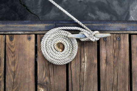 curled white rope securing boat to wooden dock の写真素材