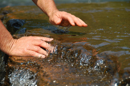 hands of a man in stream water flowing over rocks