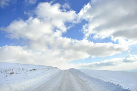 Snow covered isolated country road with beautiful clouds and blue skyの写真素材