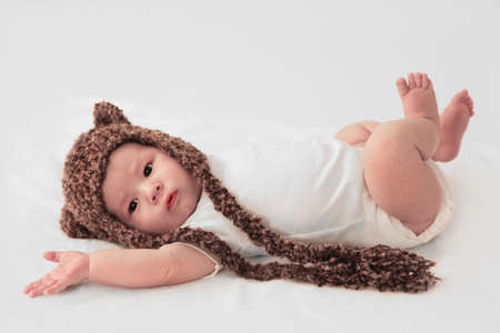 cute infant boy in white with knitted bear hatの写真素材