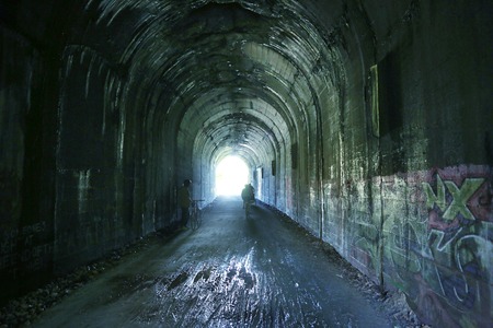 Old railway tunnel converted on walking and biking path with light at the end of the tunnelの写真素材