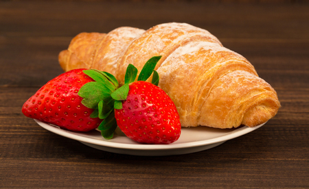 Fresh french croissant and strawberry on brown wooden table backgroundの写真素材