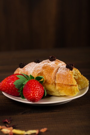 A cup of black tea with dry fruits, croissant with strawberry and wooden table backgroundの写真素材