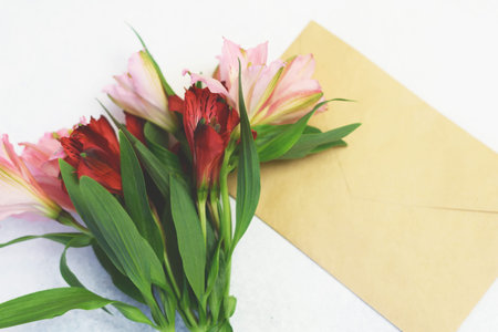 Bouquet of red and pink alstroemeria flowers and craft paper postal envelope on a white background....