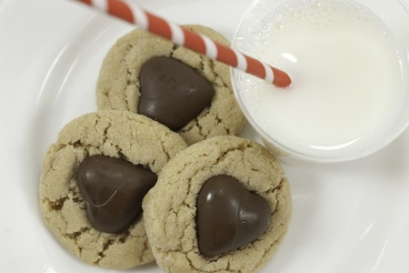 three cookies with chocolate hearts and glass of milk with a striped red straw view from above with white backgroundの写真素材