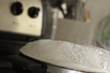 steaming pot of boiling water on stove with steam and kitchen utinsels in background shallow depth of fieldの写真素材
