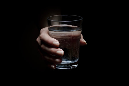 Woman holds a glass of water  Give a glass of water  Drink more water  Black background 